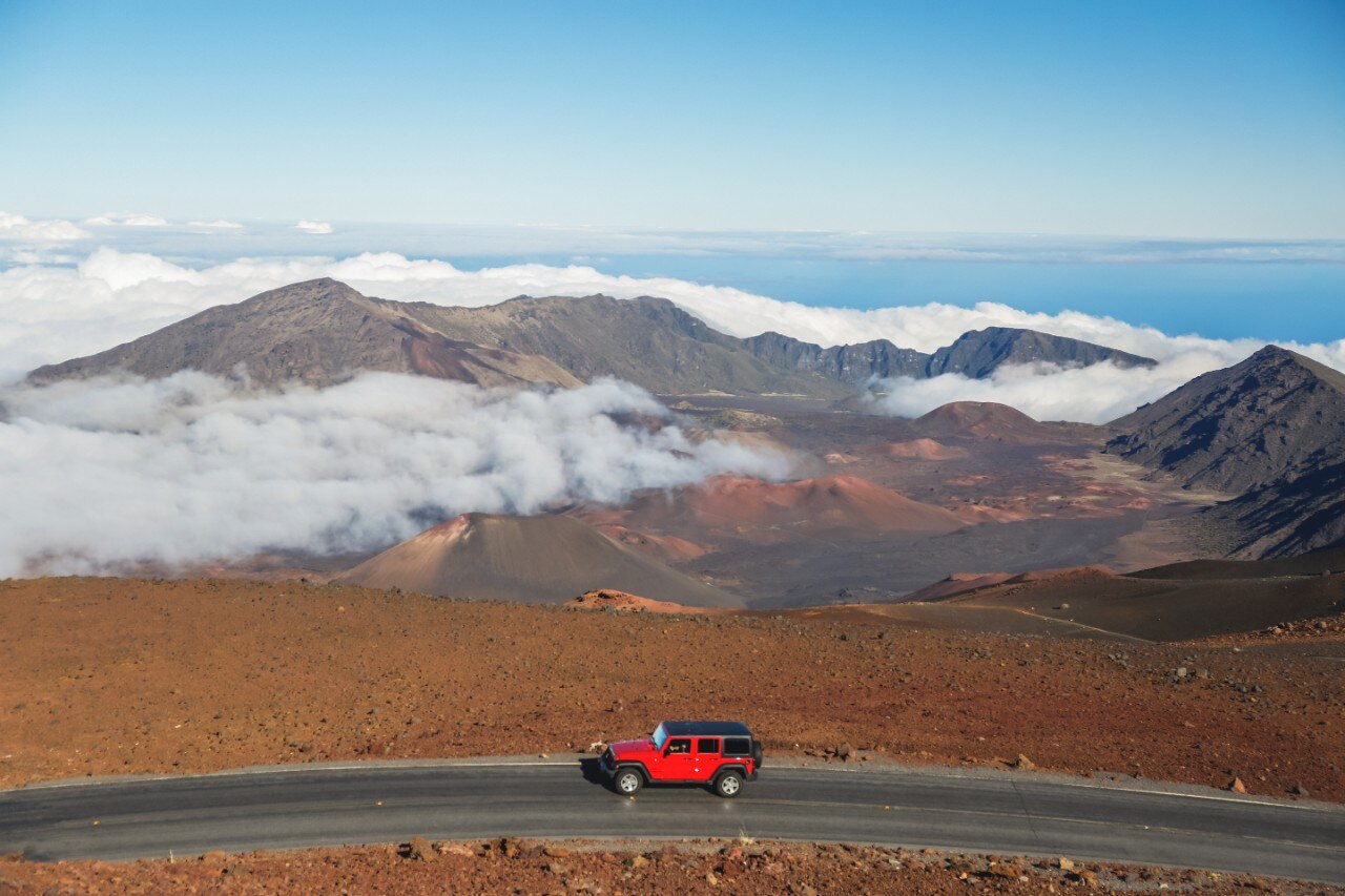 The volcanic landscape of Haleakala National Park with a red car passing, Maui, Hawaii, USA.