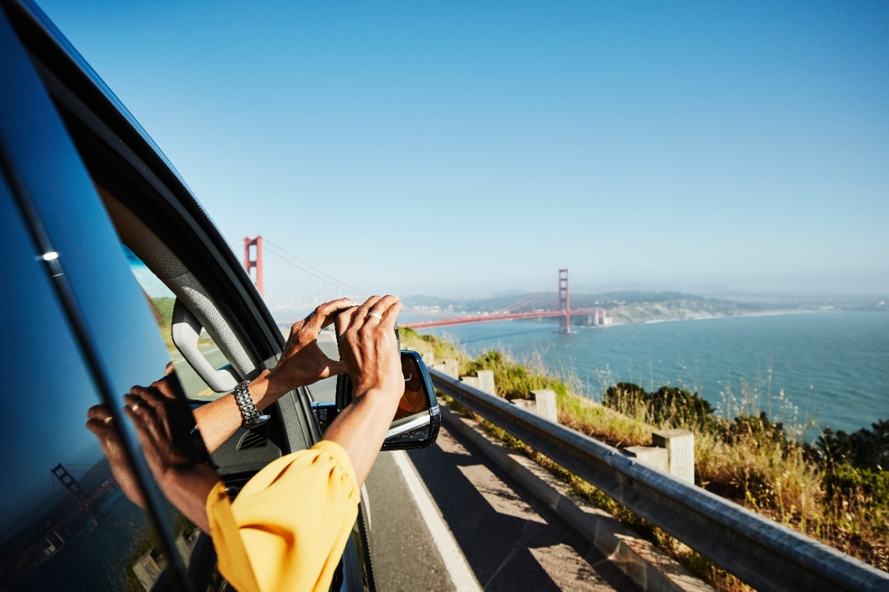 Woman taking photo of Golden Gate Bridge out of car window with smartphone